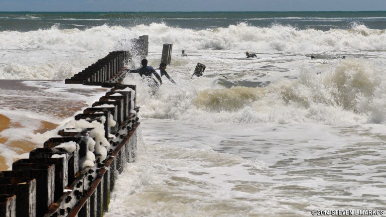 Surfers at Old Lighthouse Beach using the sea wall to help get out to the waves, Cape Hatteras National Seashore