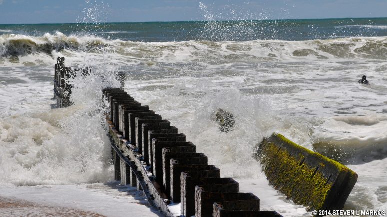Waves crash over the sea wall at Old Lighthouse Beach as a surfer tries to catch a wave, Cape Hatteras National Seashore